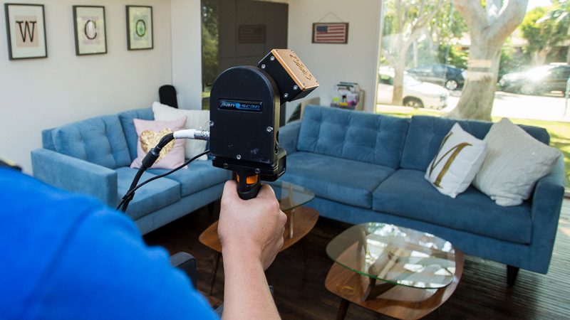 Image of 3D laser scanner capturing point cloud data in a residential living room during an As-Built survey site visit.